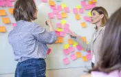 Two people talk in front of a whiteboard covered with sticky notes