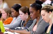 Five students sit in a row at their desk and completing an assignment on their computers