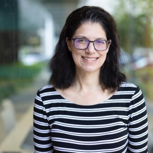 Alisa Perren Profile Picture, Black and white striped shirt, black shoulder-length hair and glasses, out-of-focus green backgrounnd