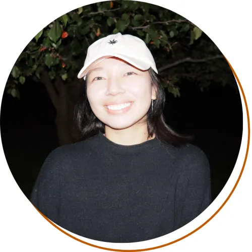 Yuqi Sun Headshot, black shirt and pink hat at nighttime, tree in the background