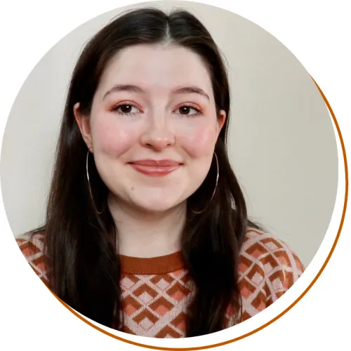 Morgan Stone Headshot, shoulders up, long dark hair, earrings, and orange patterned sweater